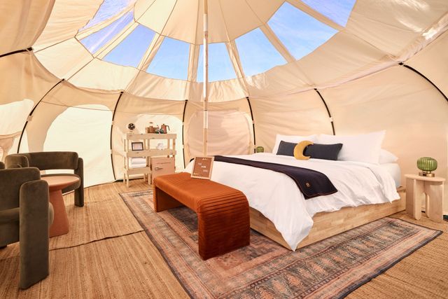 Beige glamping tent interior with bed, bench, and sitting area. Skylight windows.
