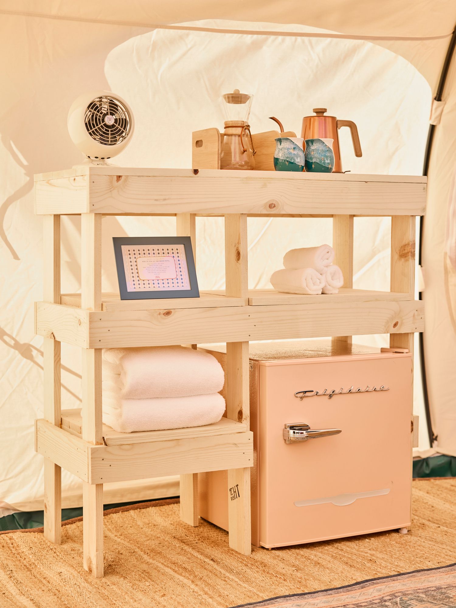 Wooden toy kitchen set with shelves, a pink mini fridge, dishes, and folded towels in a cozy room