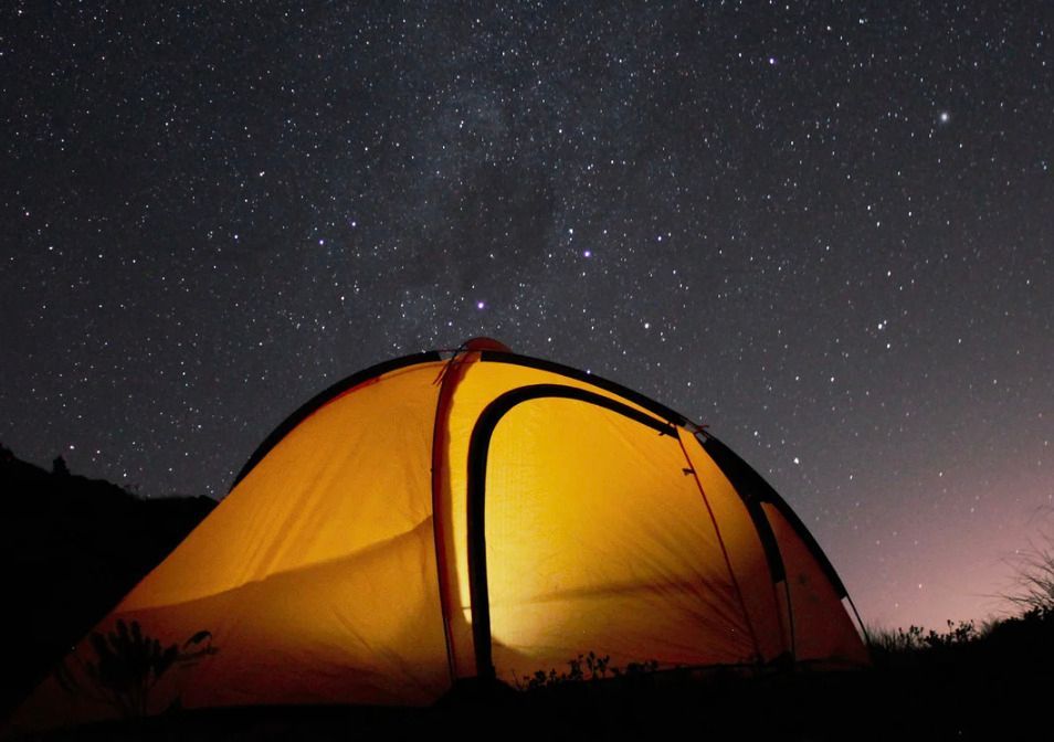 Camping tent set up on red dirt, with mountain backdrop and sparse vegetation.