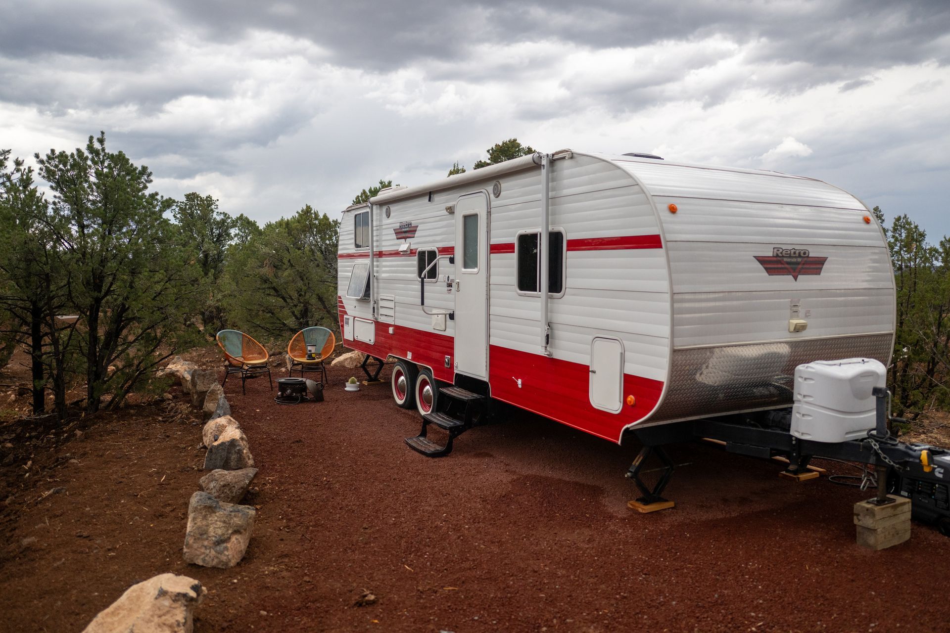 White and red travel trailer in a rocky campsite with trees and cloudy sky