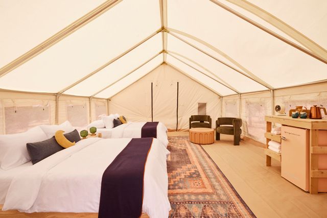 Spacious glamping tent interior with two beds, rug, desk, and sitting area