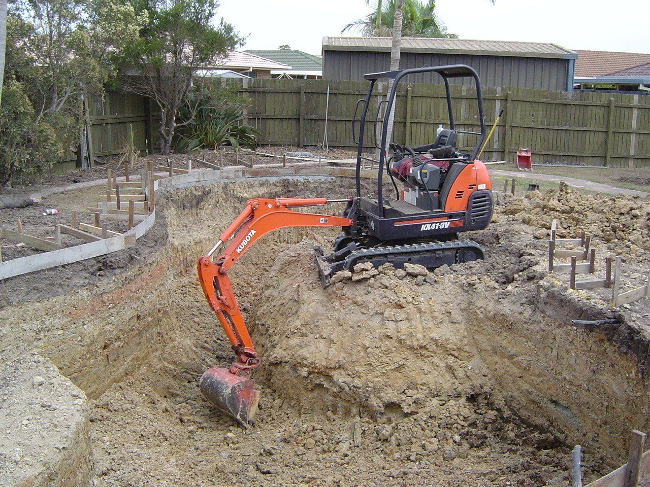 Mini excavator digging in a dirt pit at a construction site. Orange and black machine.