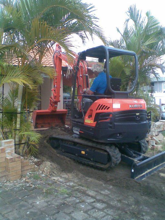 Orange and black Kubota mini-excavator digging near a house, operated by a person.
