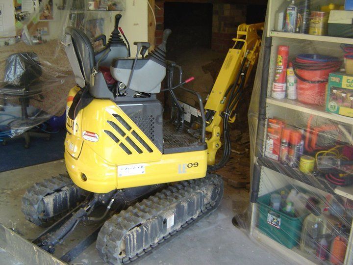 Yellow mini excavator inside a room with shelves.