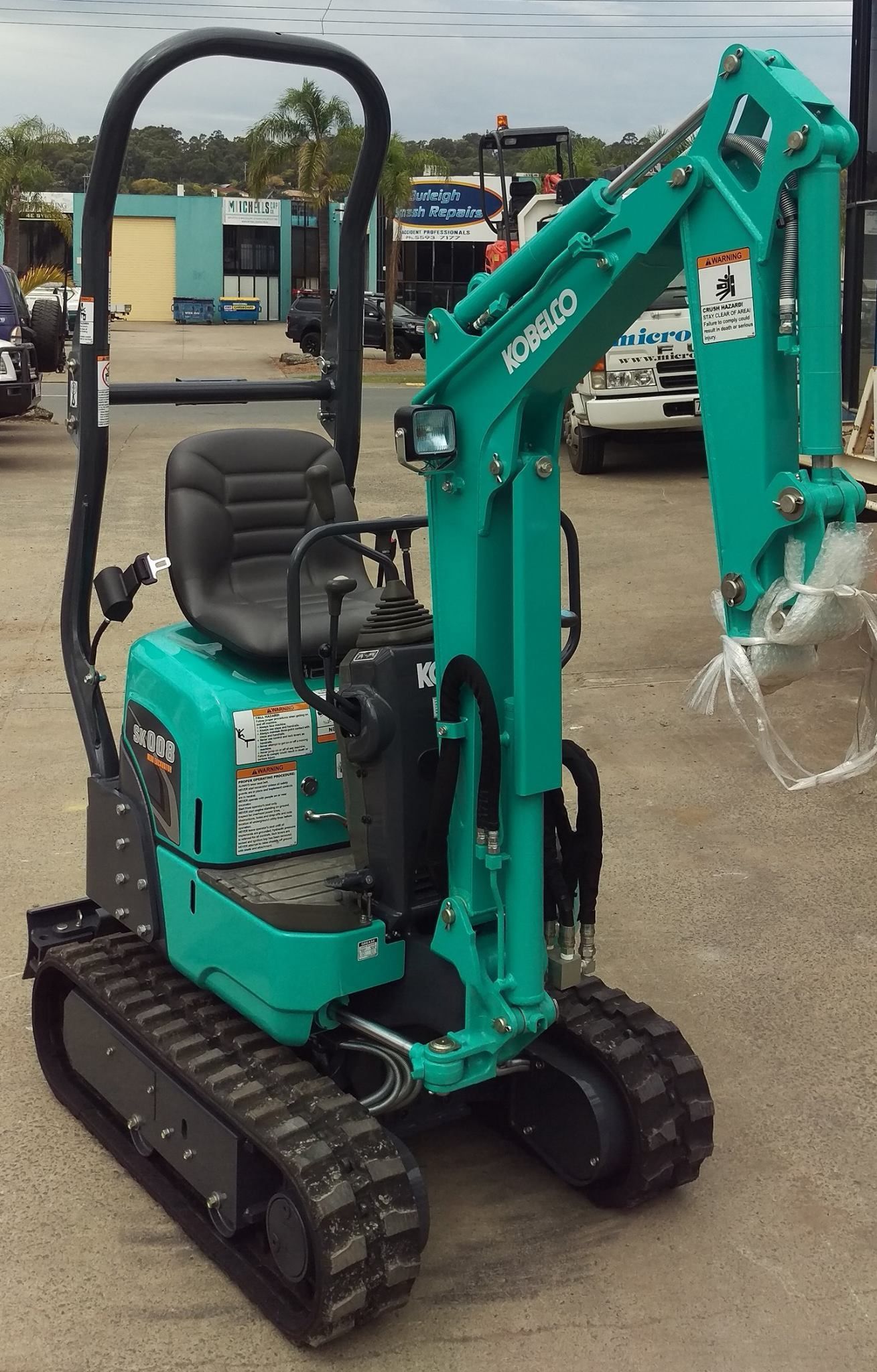 A teal mini excavator with black tracks, seat and roll bar on a paved surface.