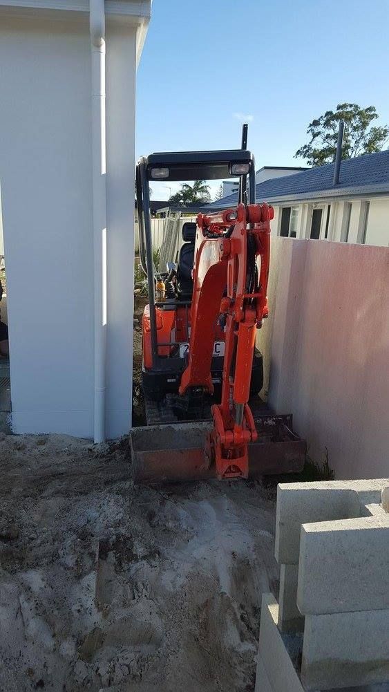 Orange excavator operating in tight space between building and wall.