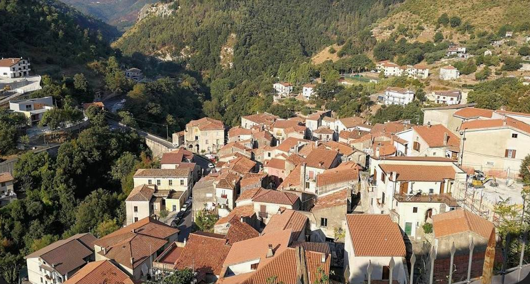 Villaggio collinare soleggiato con tetti di terracotta, incastonato tra verdi montagne