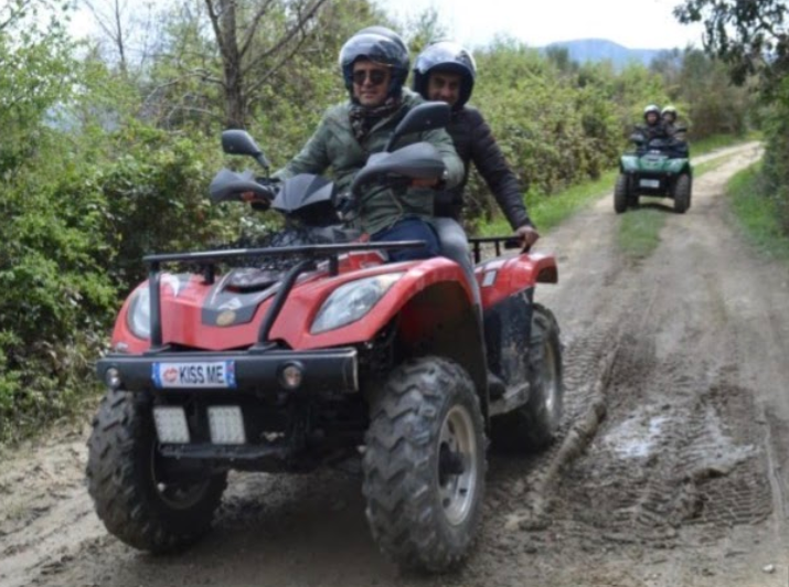 Due motociclisti su un quad rosso su un sentiero fangoso, con un altro quad alle loro spalle.