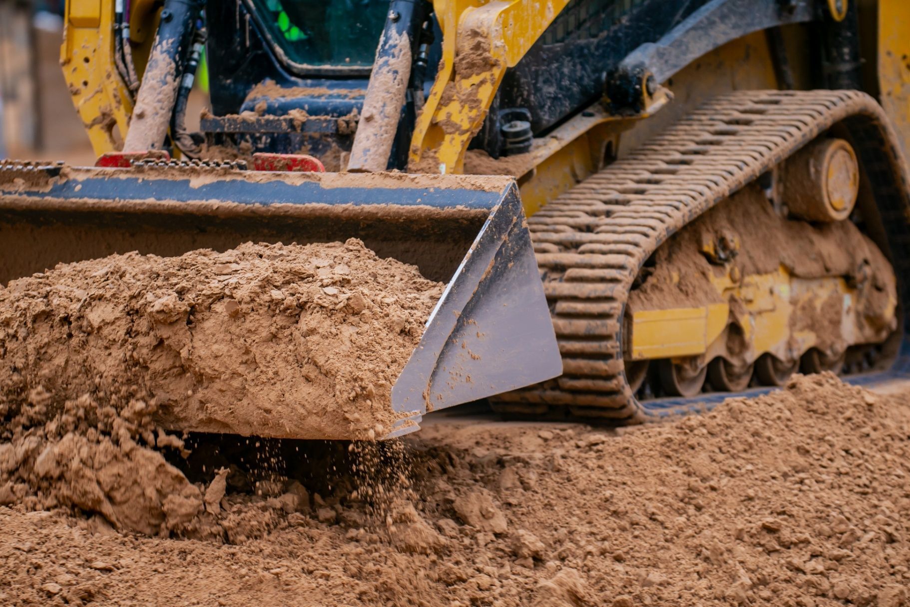 Yellow bulldozer with track treads scooping up and pushing brown earth.