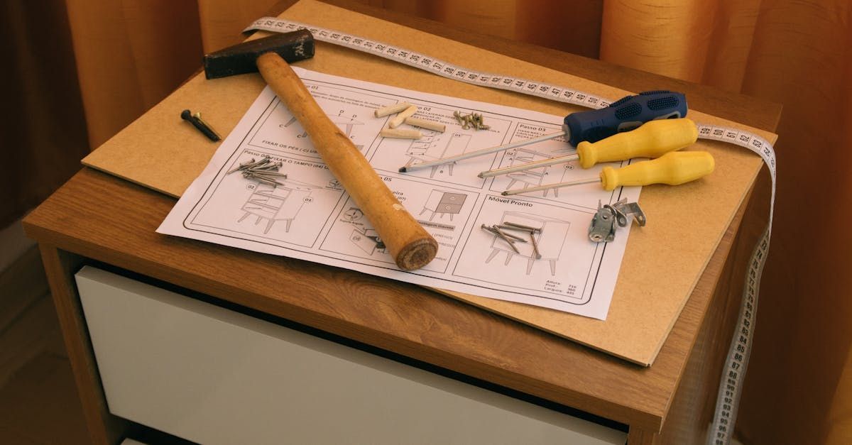 A hammer , screwdriver , and measuring tape are on a wooden table.