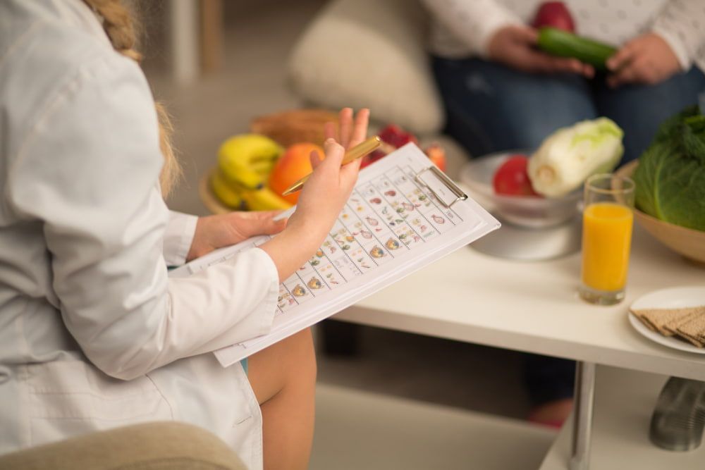 A Woman Is Sitting at A Table with Fruits and Vegetables While a Nutritionist Is Talking to Her — Tuncurry Medical Centre In Tuncurry, NSW