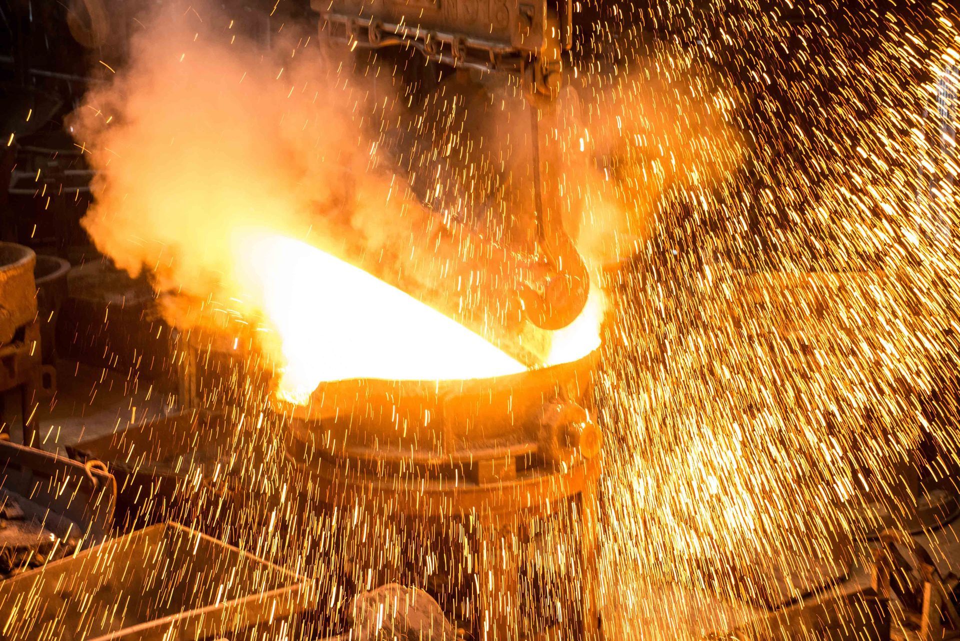 Molten metal being poured in a foundry, sending bright orange sparks everywhere