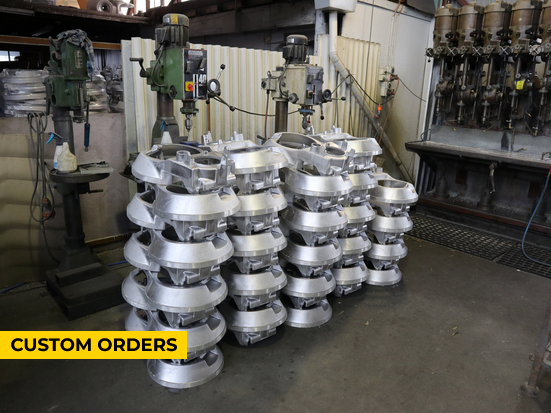 Stacks of silver metal parts in a workshop, with machinery in the background, labeled