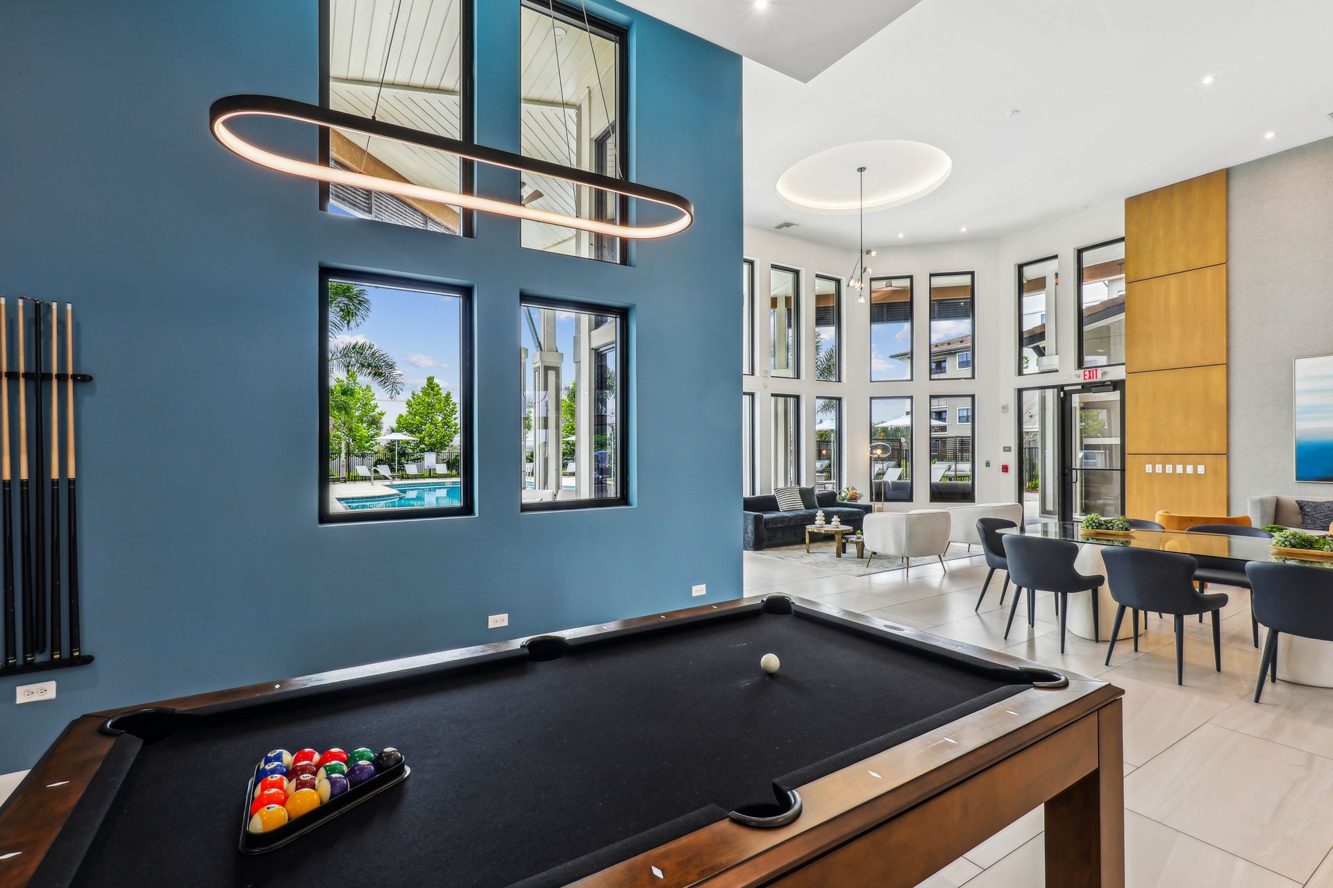 Pool table in a teal-walled room with large windows, bright lighting, and a view of a pool.