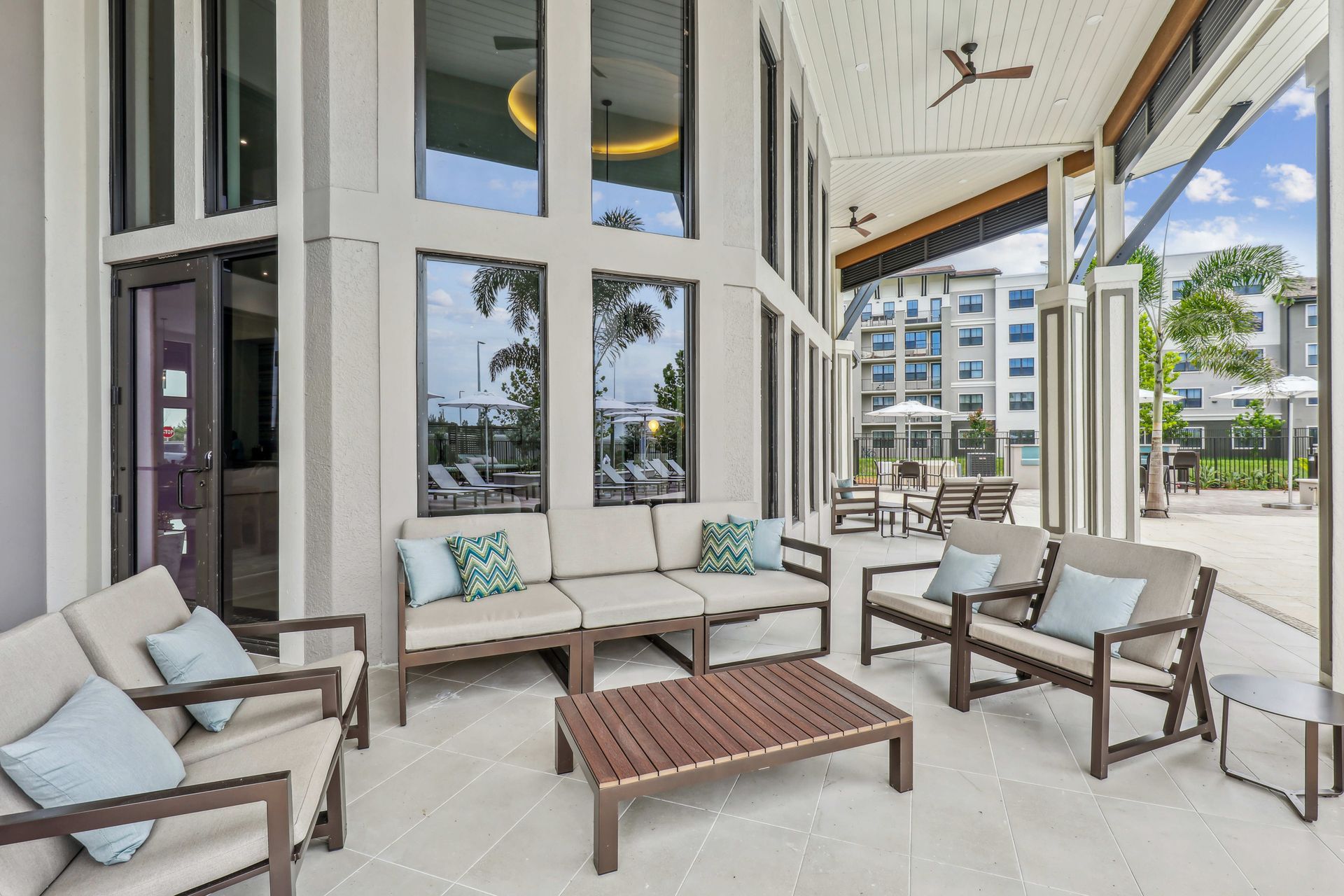 Patio with beige couches, teal pillows, wooden coffee table, and large windows.