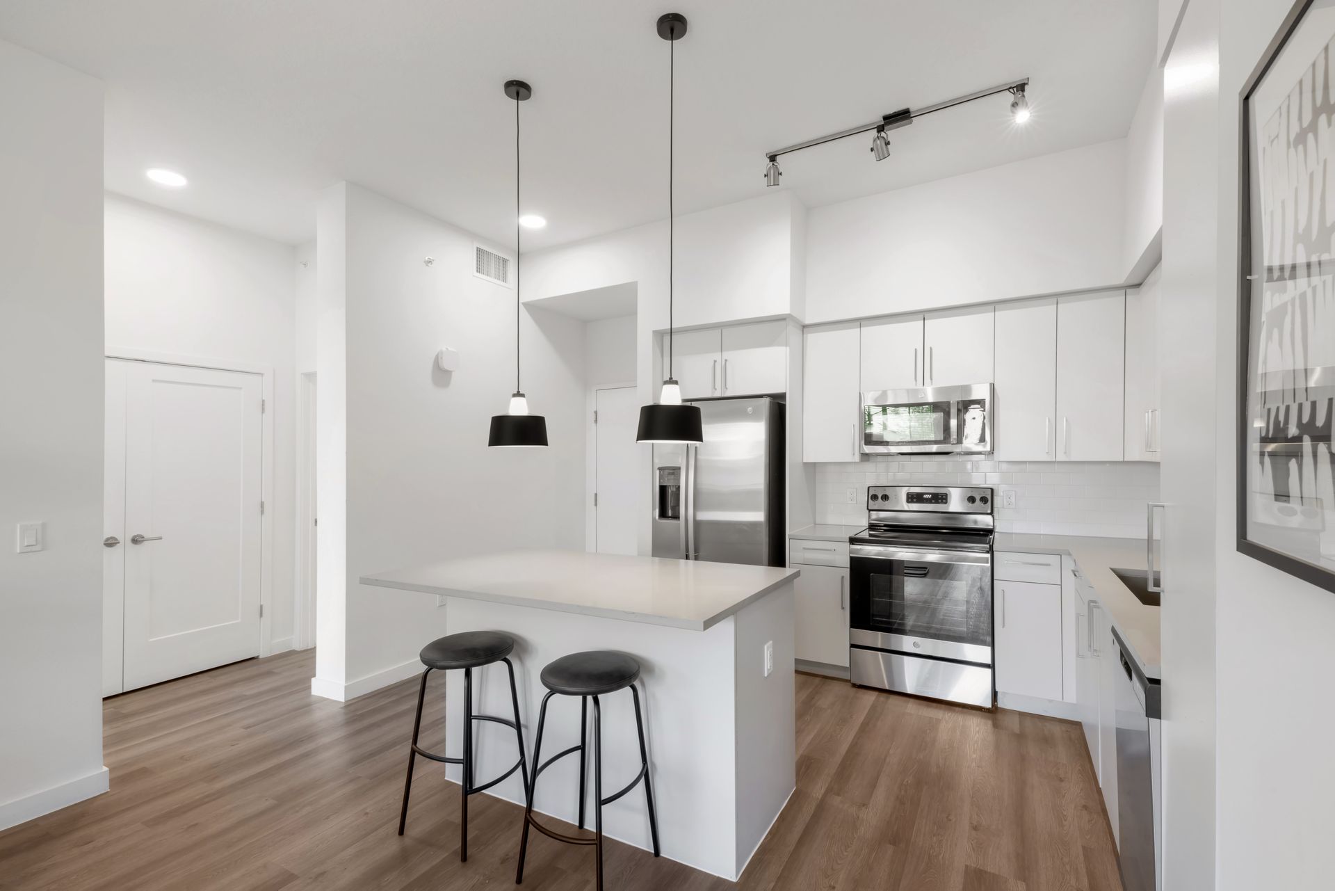 Modern white kitchen with island, stainless steel appliances, and two stools.