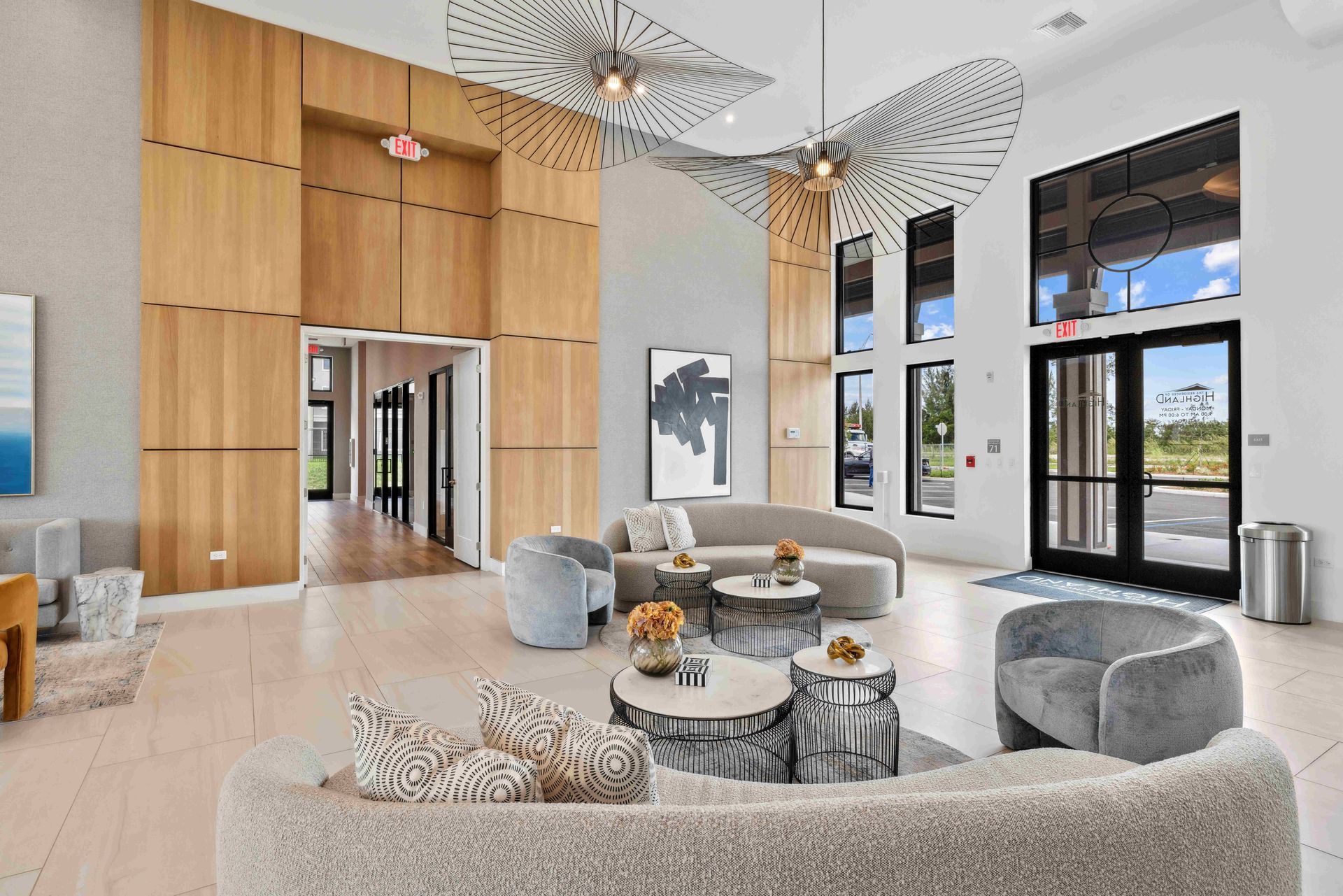 Lobby with light wood walls, curved sofa, armchairs, small tables, and large windows. Decorative ceiling art.