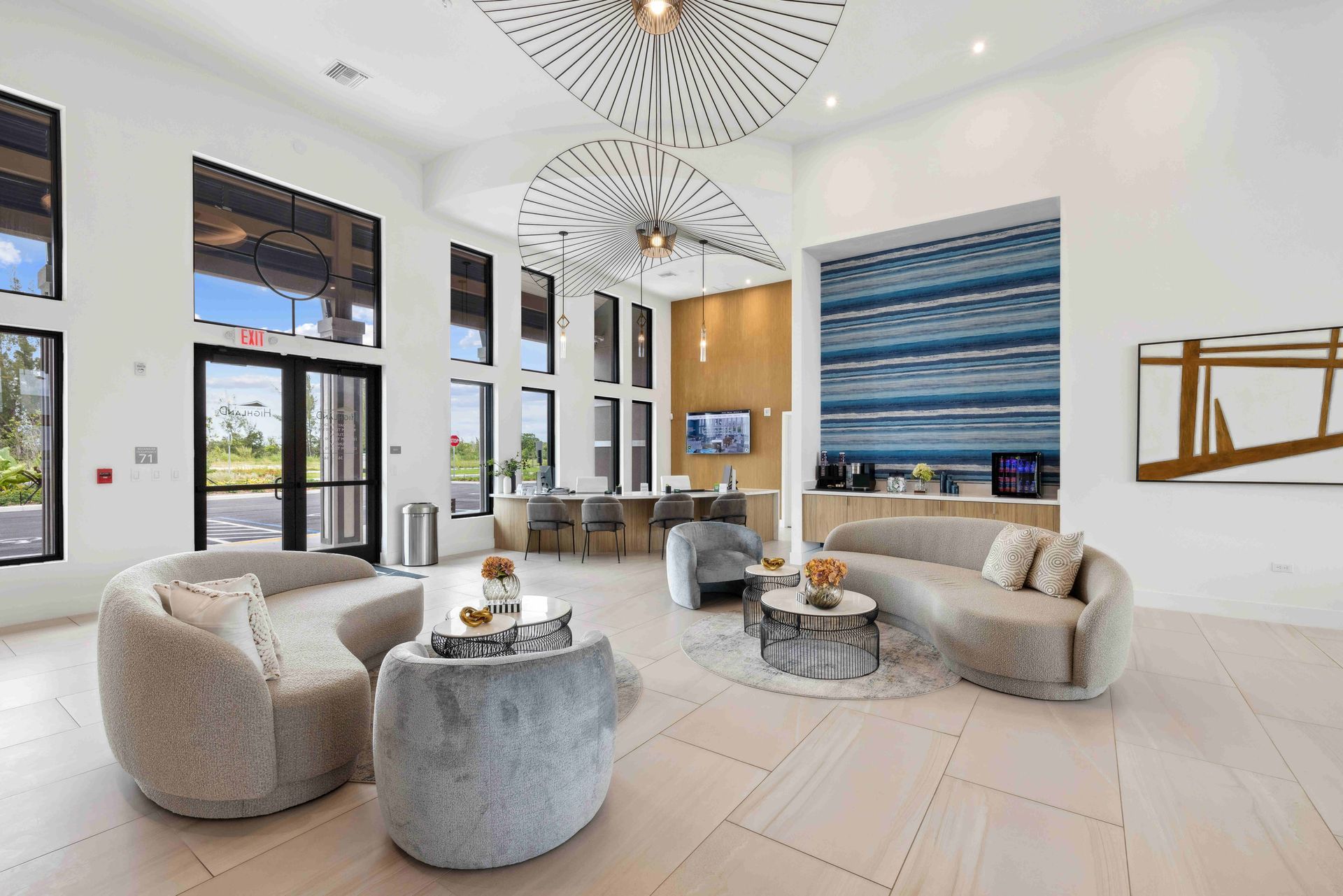 Lounge area with modern decor: curved sofas, round coffee tables, tall windows, and decorative ceiling lights.