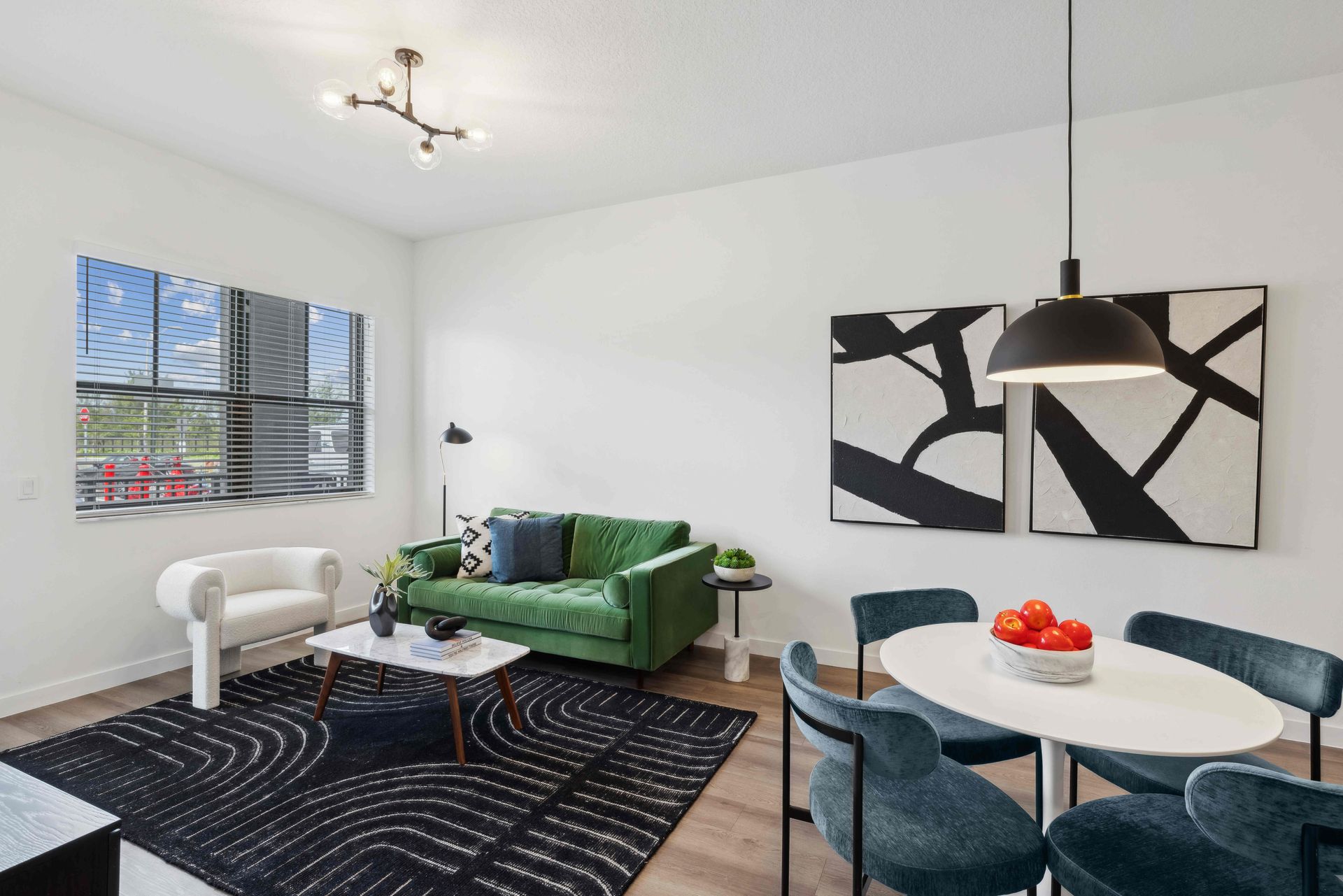 Modern living room: green sofa, white chair, black and white art, round dining table with blue chairs.