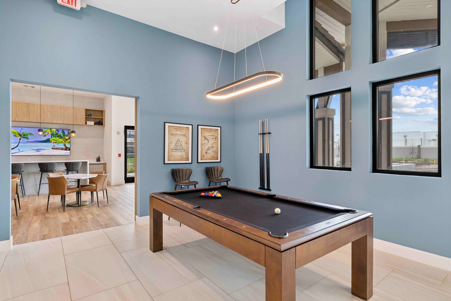 Pool table in a blue-walled room with large windows, a modern light fixture, and an adjoining lounge area.