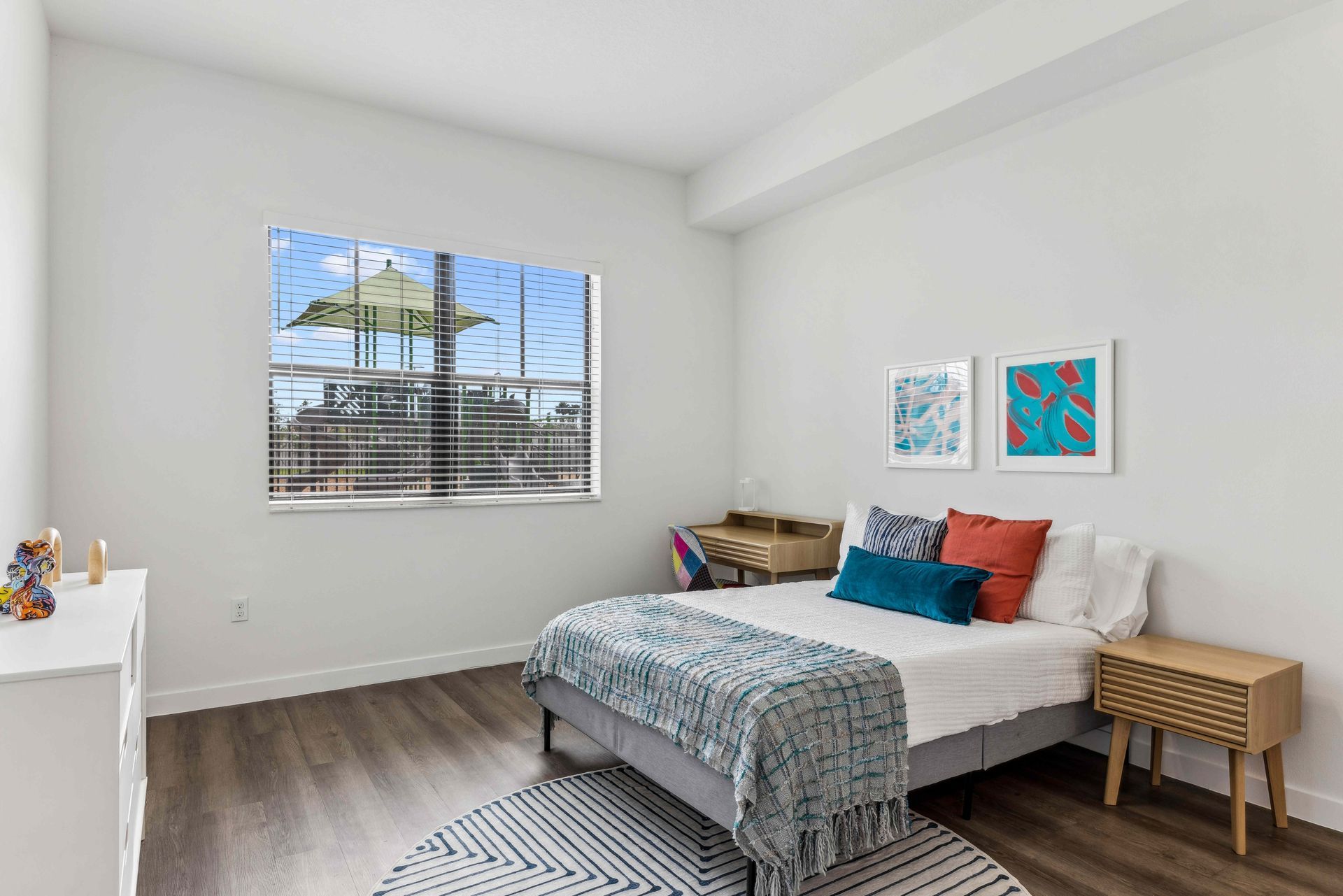 Bedroom with bed, desk, dresser, nightstand, and window overlooking a structure.