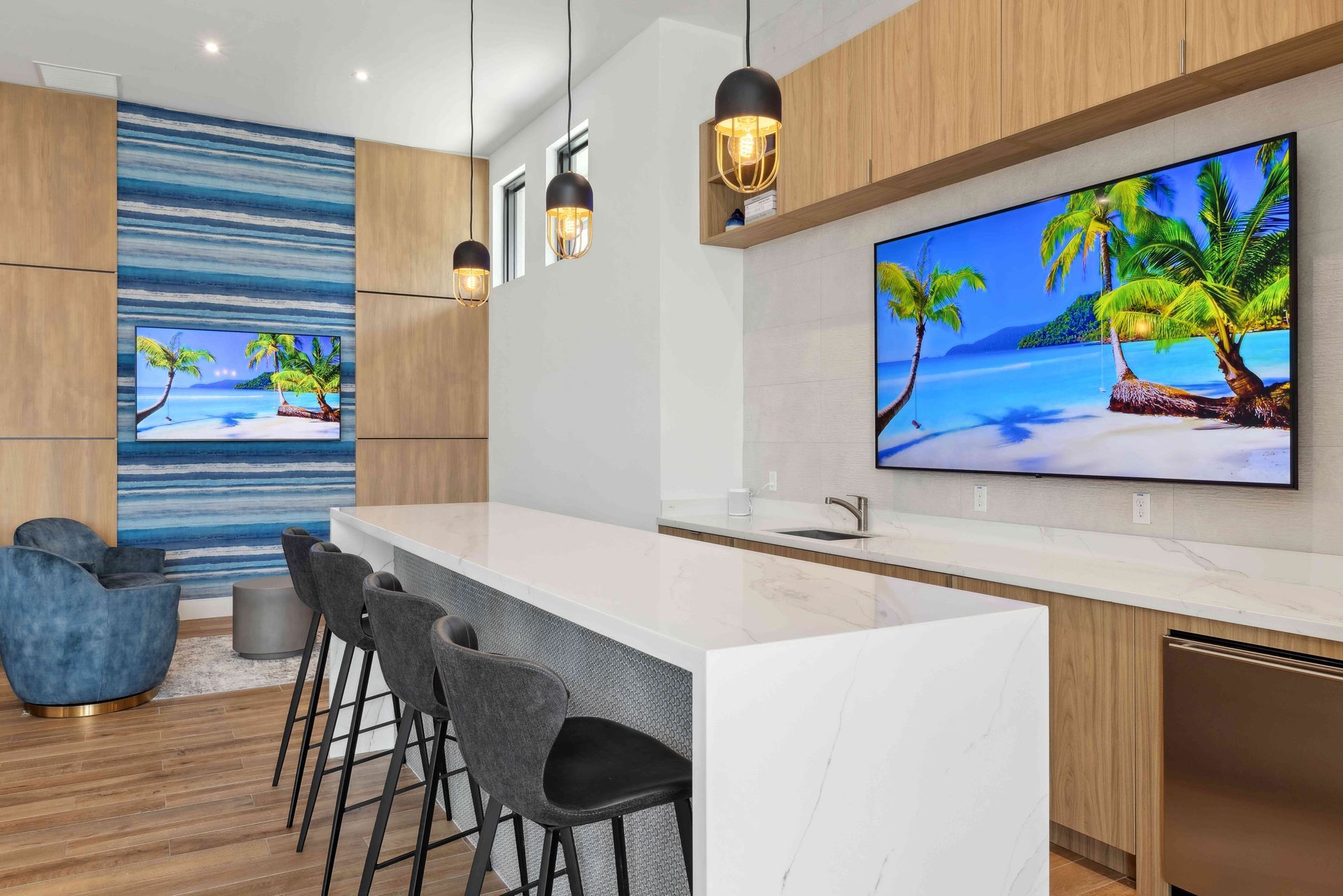 Modern lounge with bar seating, TVs showing tropical beach scenes, and light wood cabinetry.