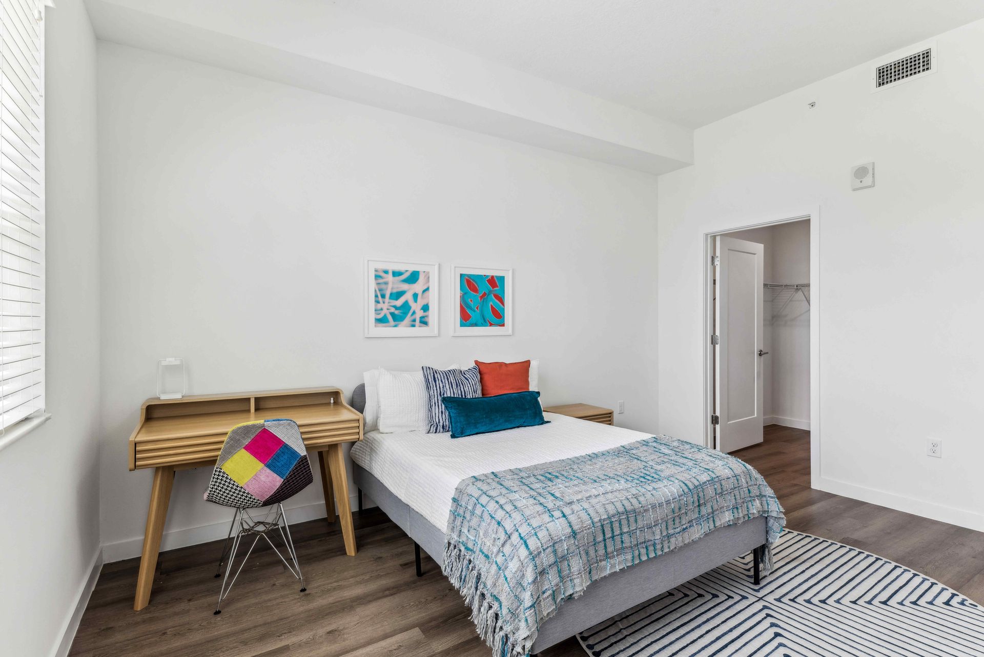 Bedroom with a bed, desk, chair, rug, and two framed pictures on a white wall.