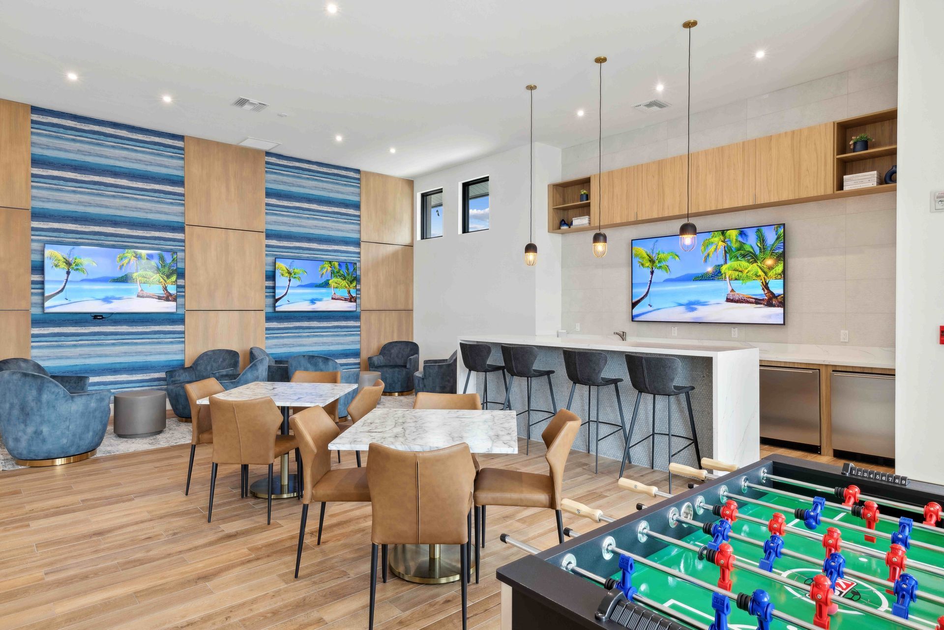 Modern lounge with foosball table, tables, chairs, TVs, and a bar area.