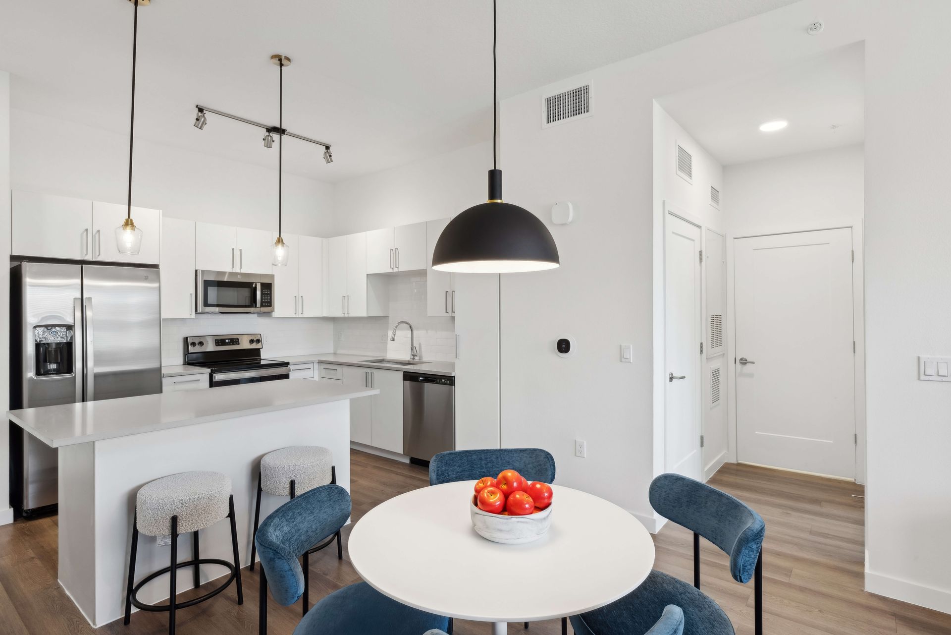 Modern kitchen with white cabinets, stainless steel appliances, and a round table with fruit.
