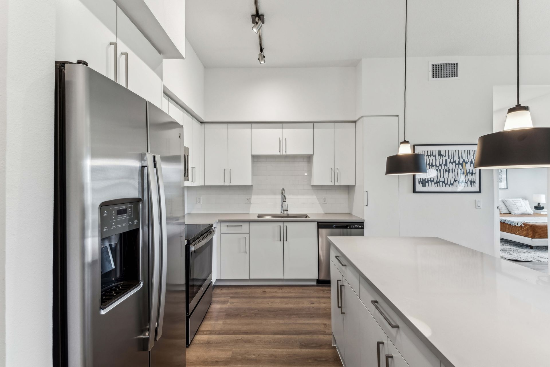 Modern white kitchen with stainless steel appliances, wood floor, and island.