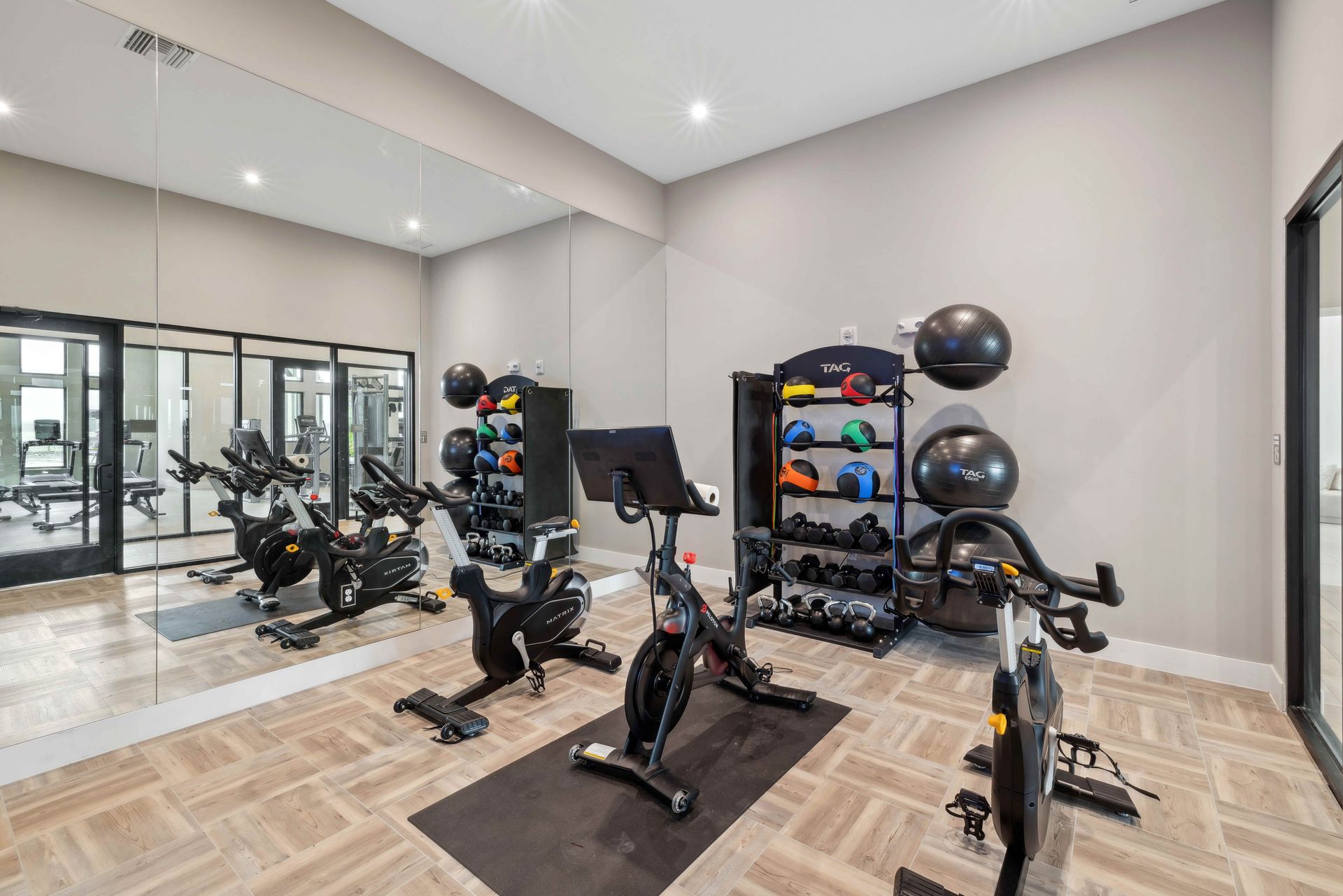Gym with exercise bikes, weights, and mirrored wall. Beige walls and flooring.