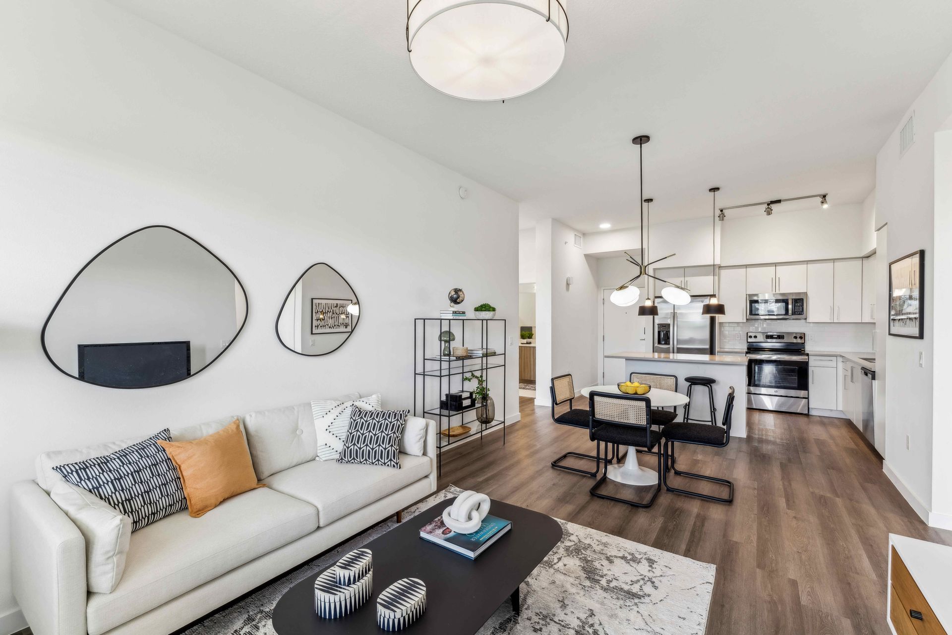 Modern apartment living room with white walls, open kitchen, and neutral furniture.