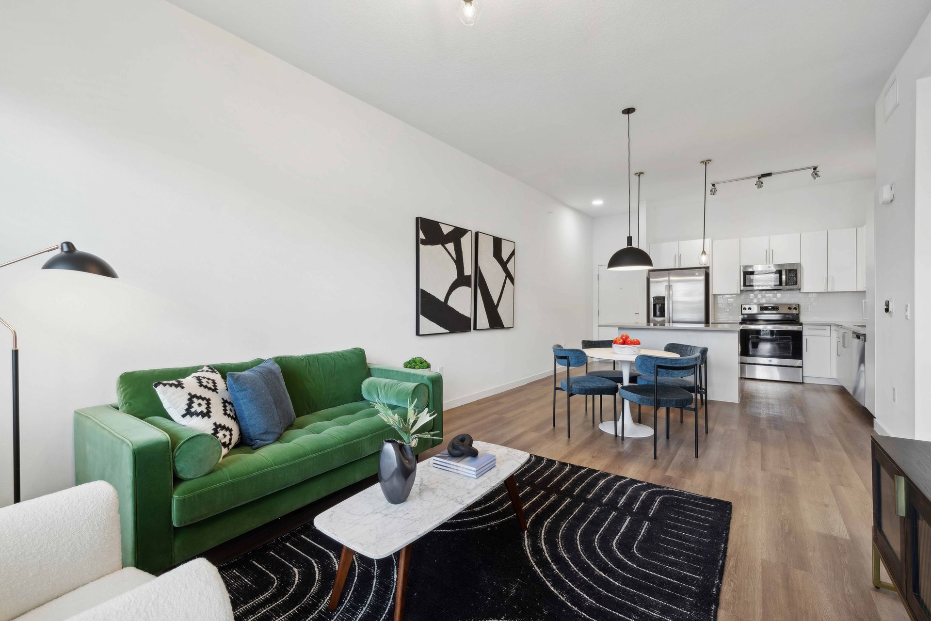 Modern apartment interior: green sofa, white kitchen, dining table, black rug.