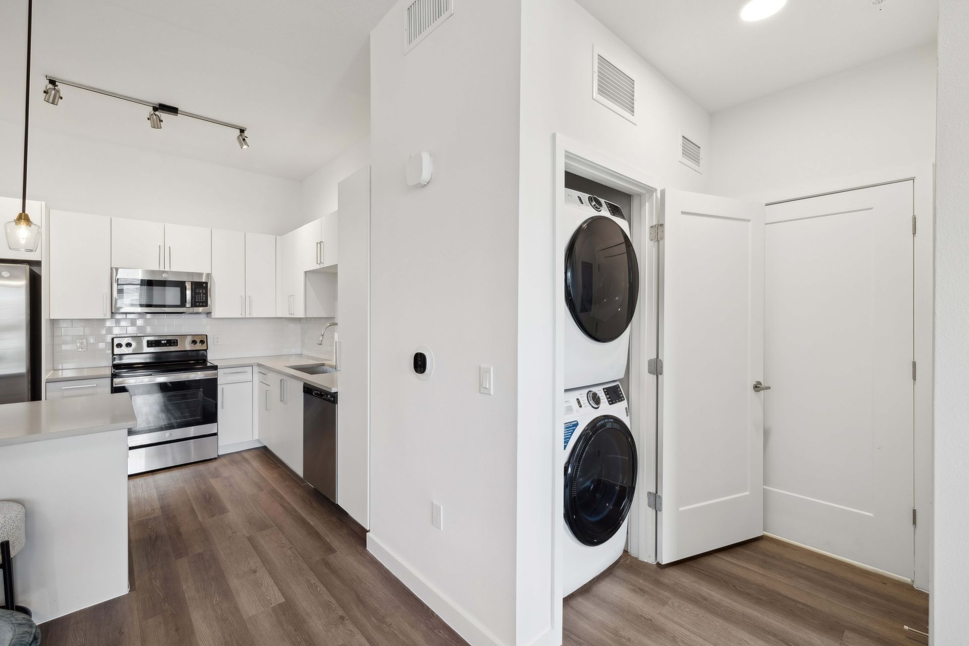Modern apartment interior with kitchen, laundry closet, and wood flooring. Bright white walls.