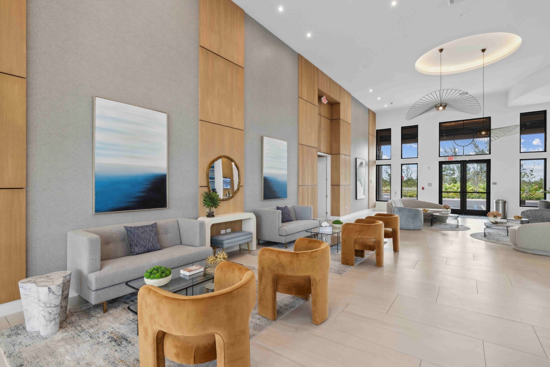 Spacious modern lobby with light wood panels, sofas, art, and high windows overlooking a green outdoor space.