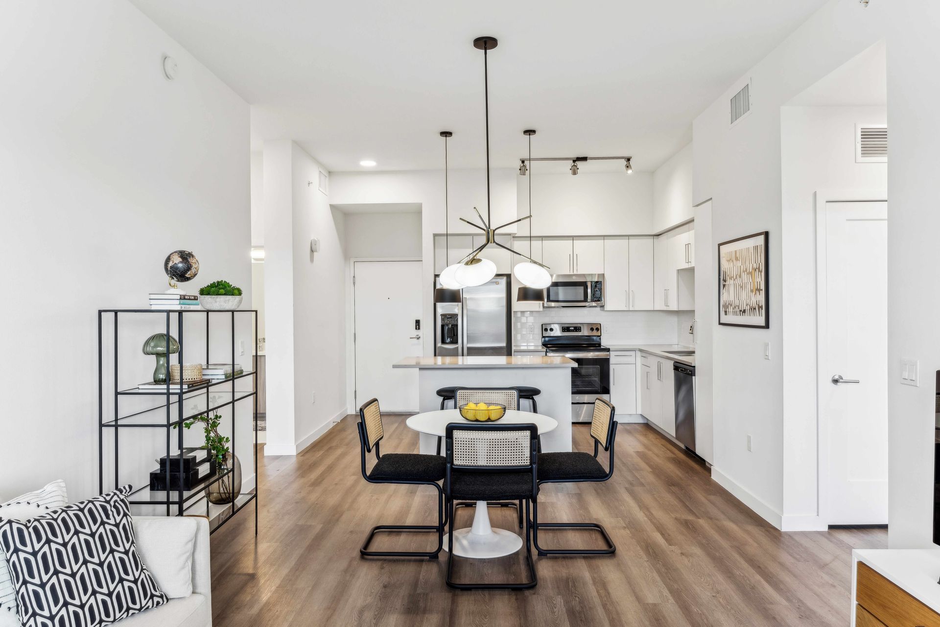 Modern open-plan kitchen and dining area with white walls, wood floors, and minimalist furniture.