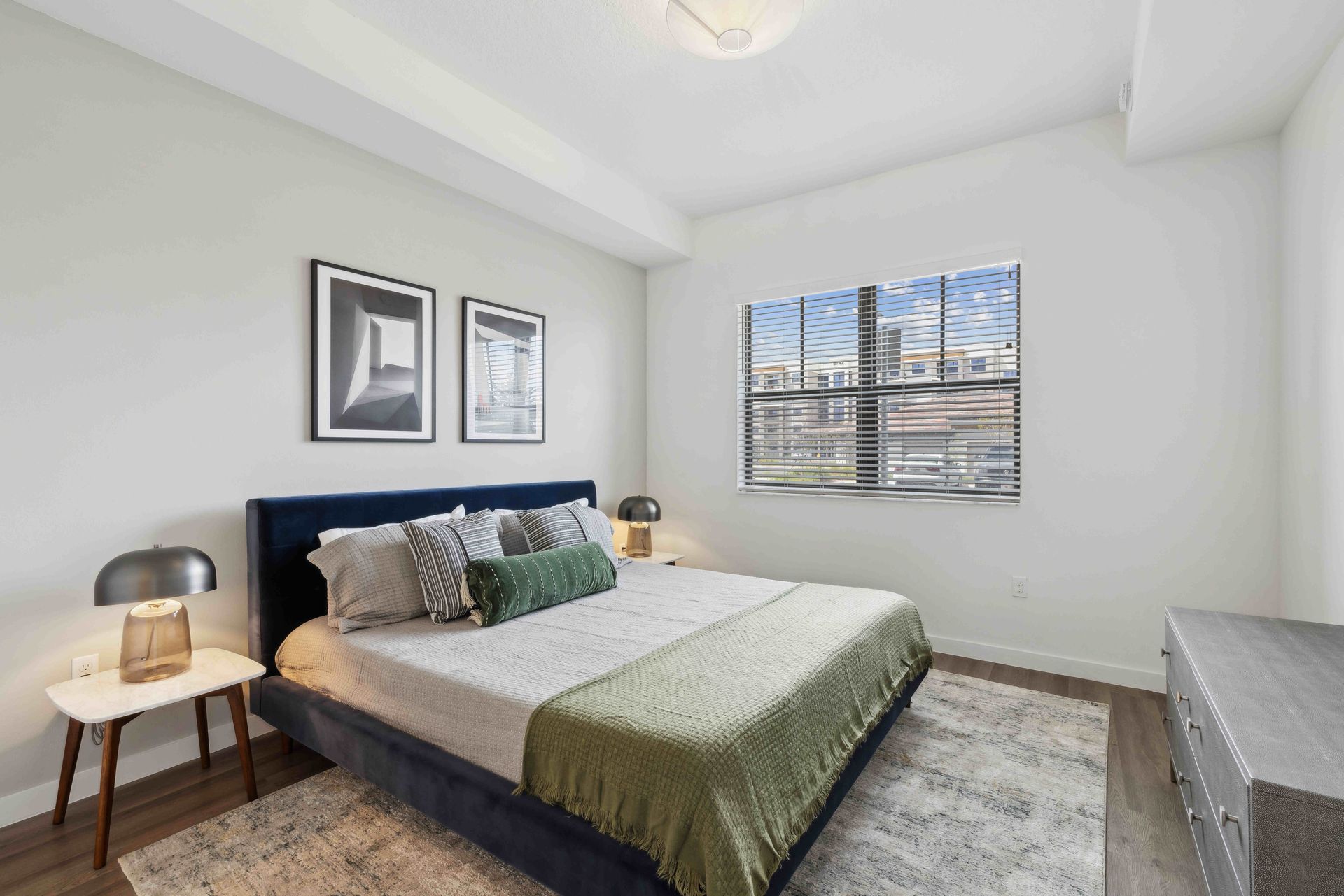 Bedroom with a blue bed, two framed pictures, a window, and a gray rug.