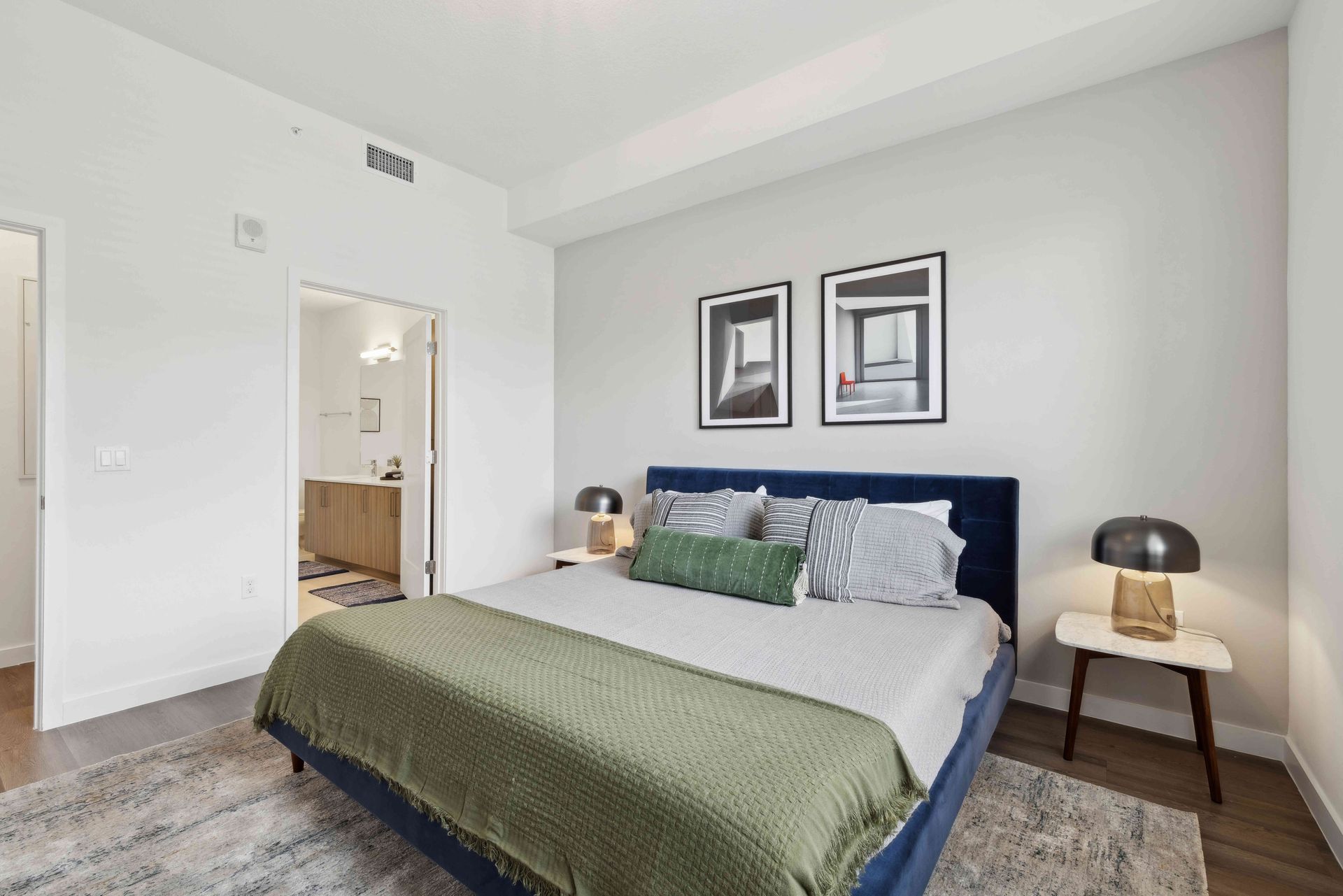 Bedroom with a blue bed, green blanket, gray rug, and two framed pictures.