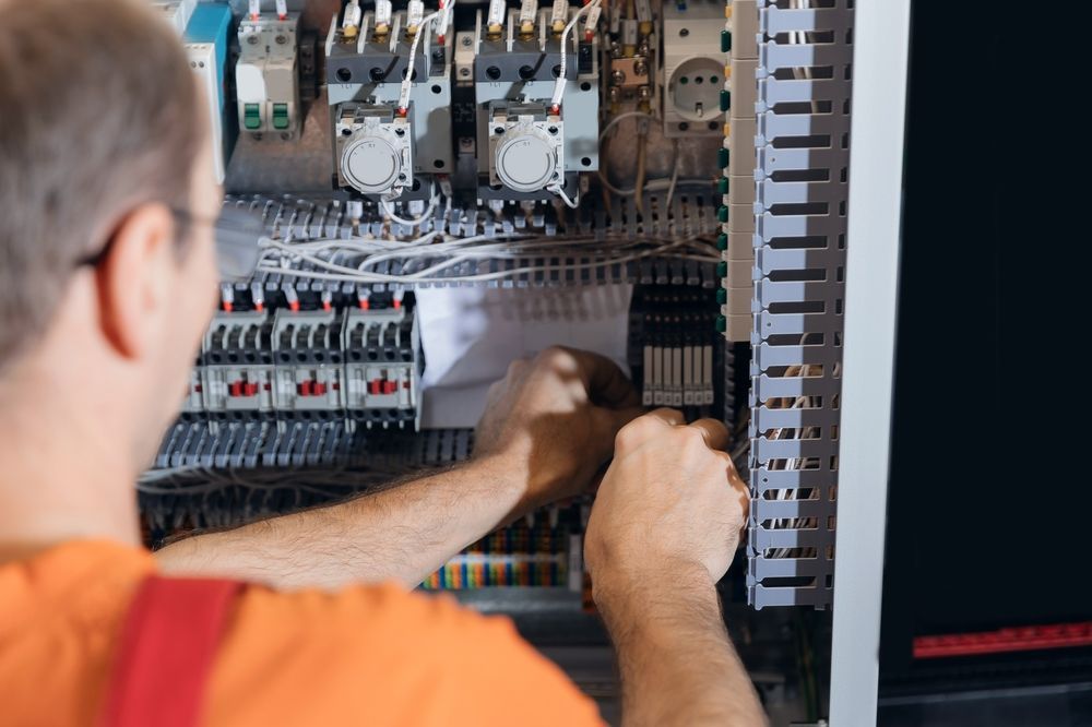Technician wiring an electrical control panel with tools inside an open cabinet