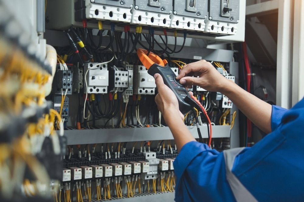 Technician using a multimeter to inspect wiring inside an electrical control panel