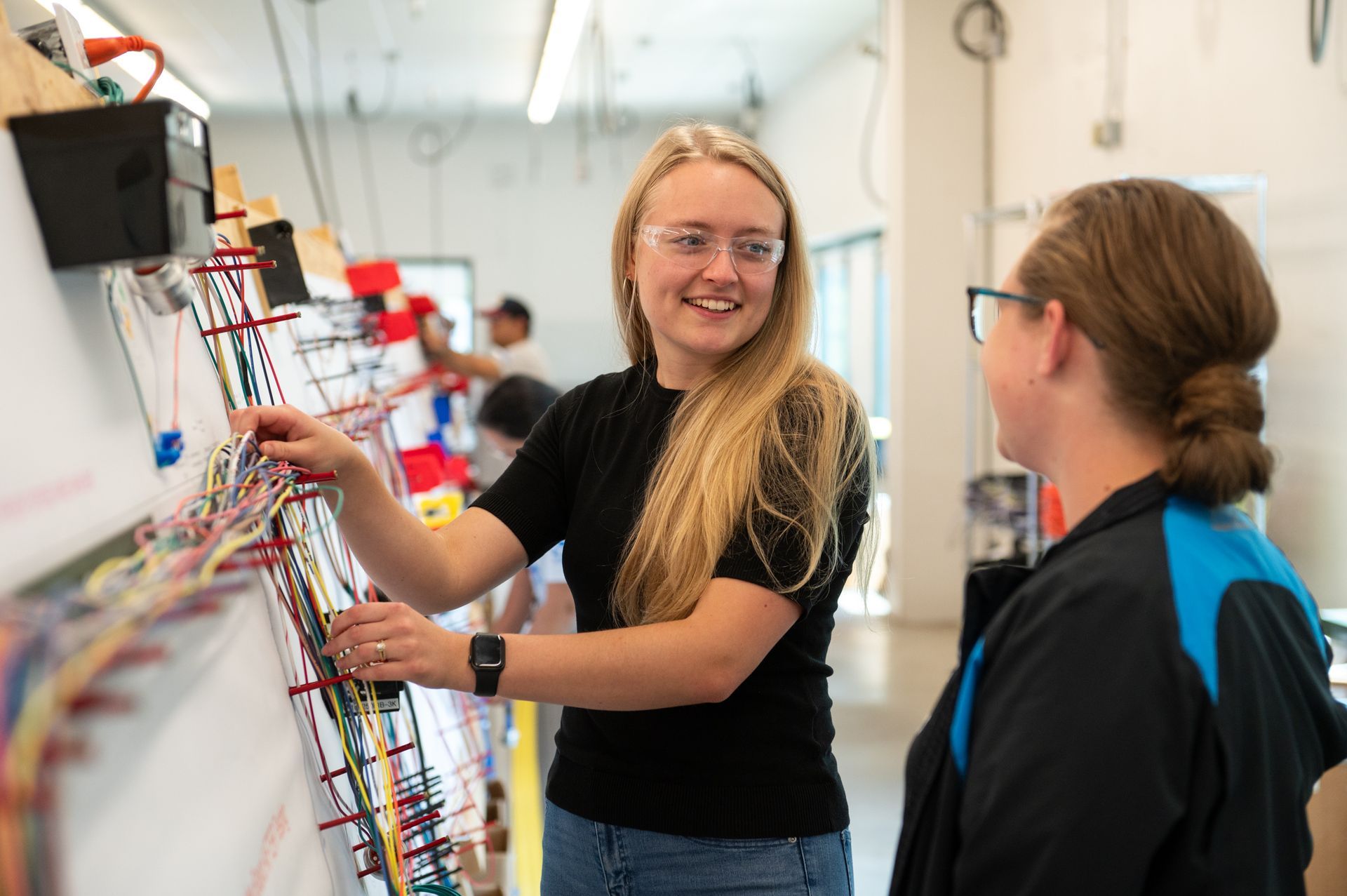 Two female Kato Cable technicians inspecting a wiring board.