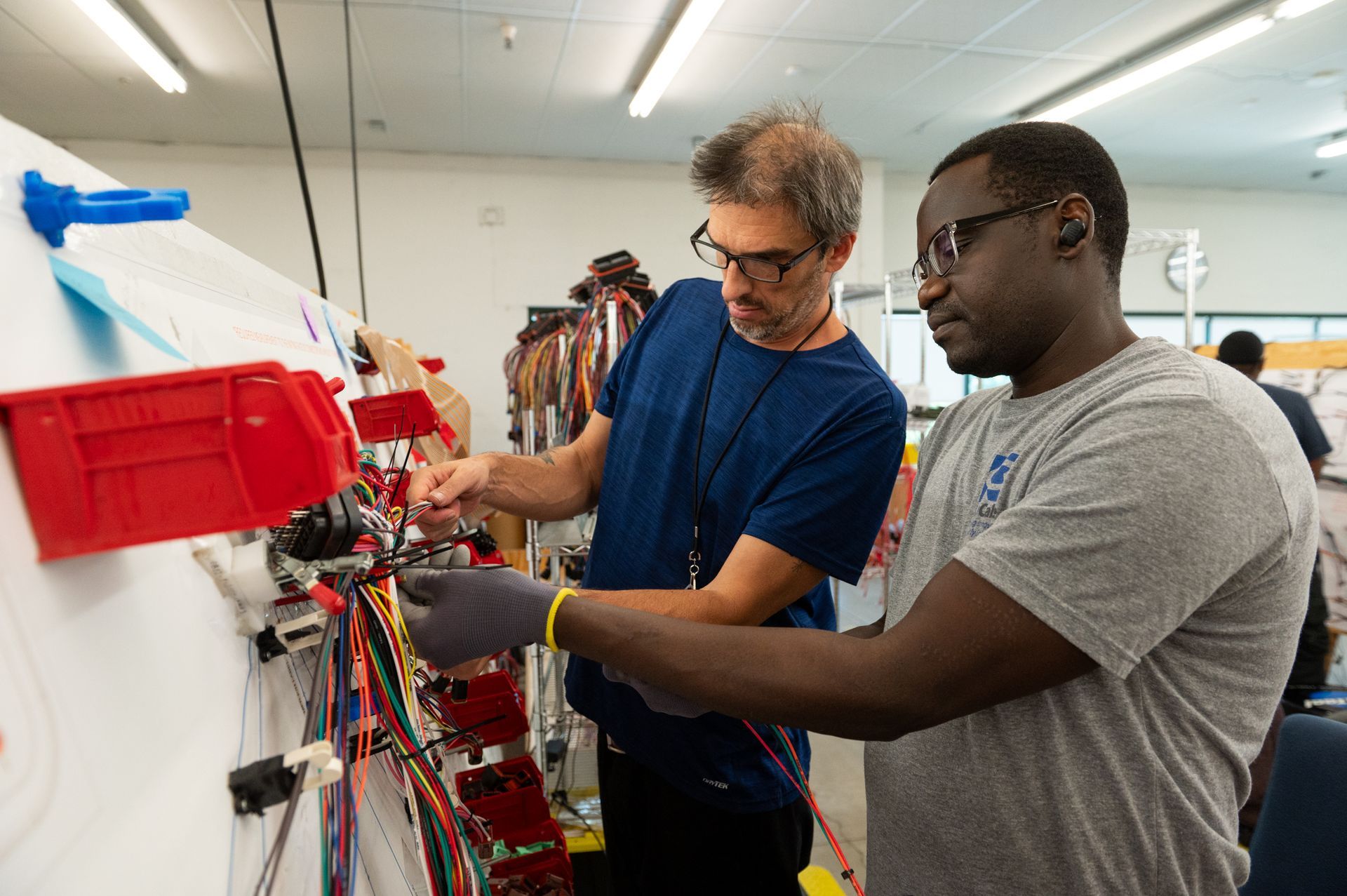 Two male Kato Cable technicians inspecting a wiring board.