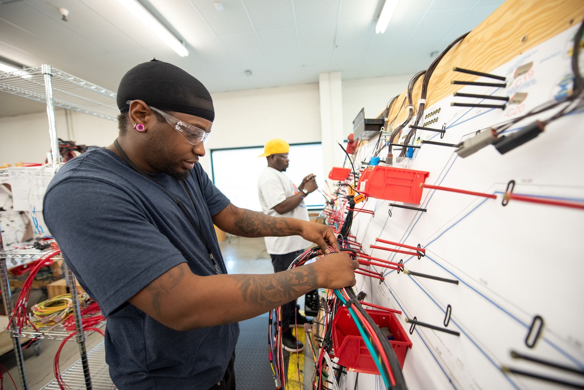 A male Kato Cable technician standing next to a wiring board, working.