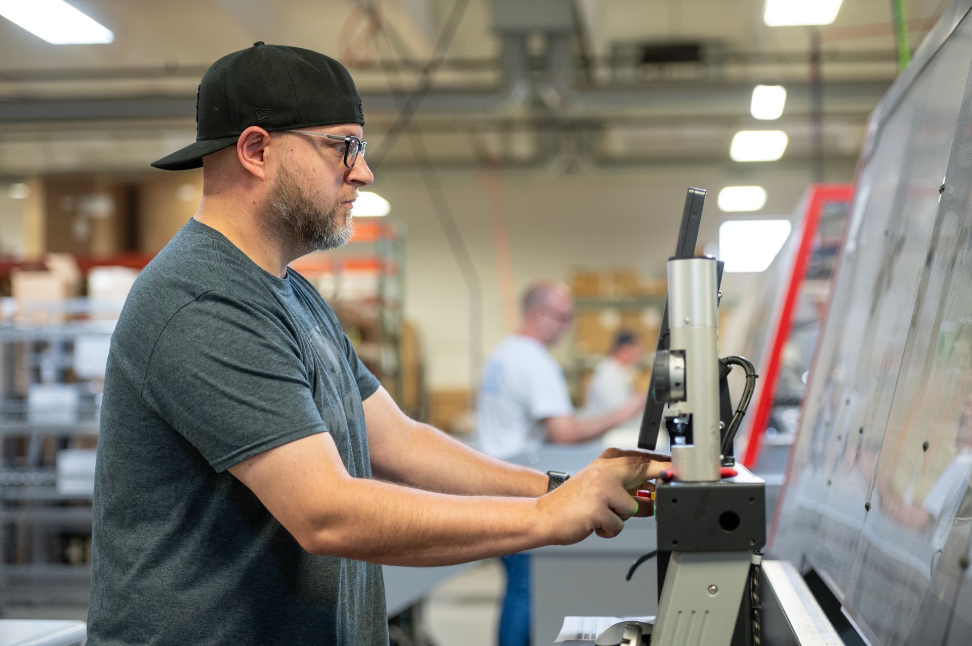 A Kato Cable technician standing next to a wiring machine, working.