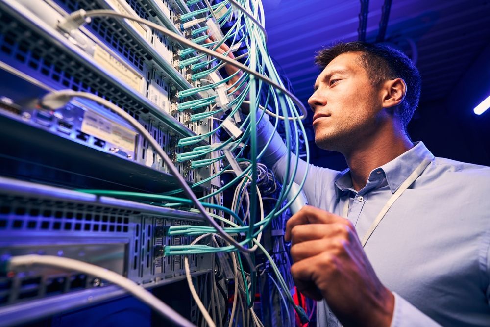 Man examining network cables in a server room, focused expression, blue and green cables.