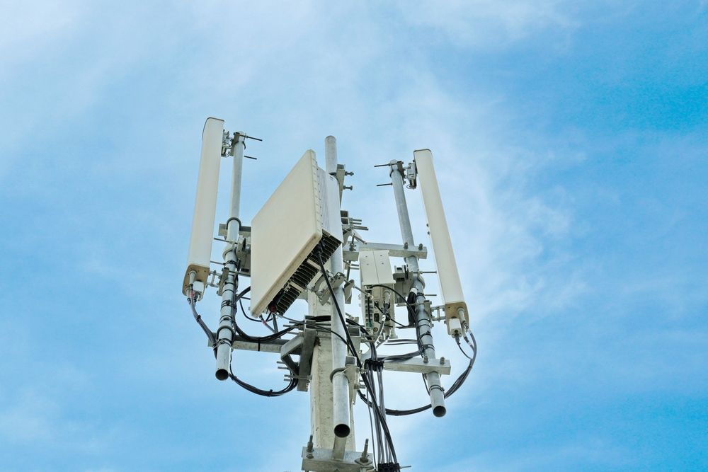 A cellular communication tower with multiple panel antennas and equipment mounted against a bright blue sky.