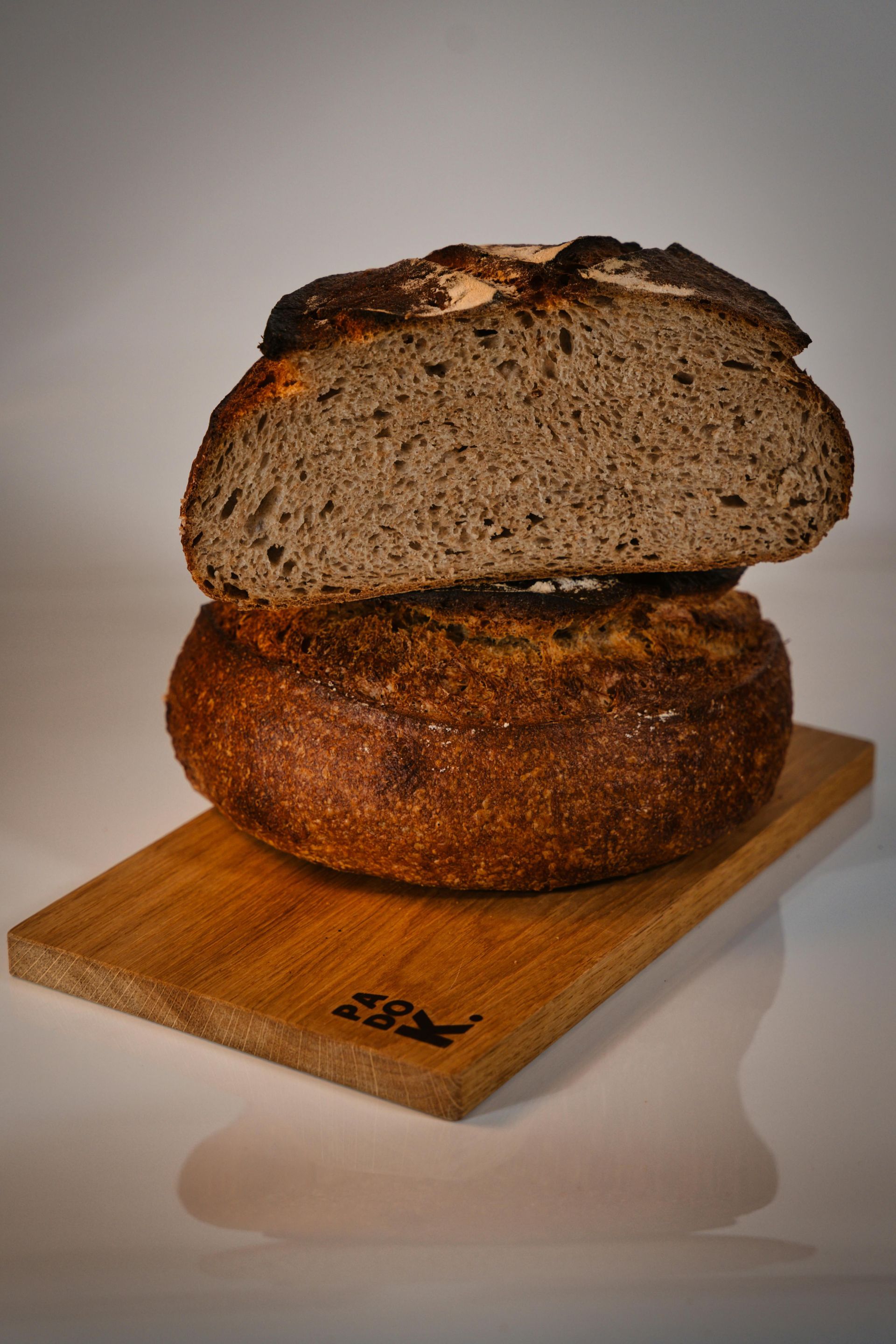 Two loaves of bread are stacked on top of each other on a wooden cutting board.