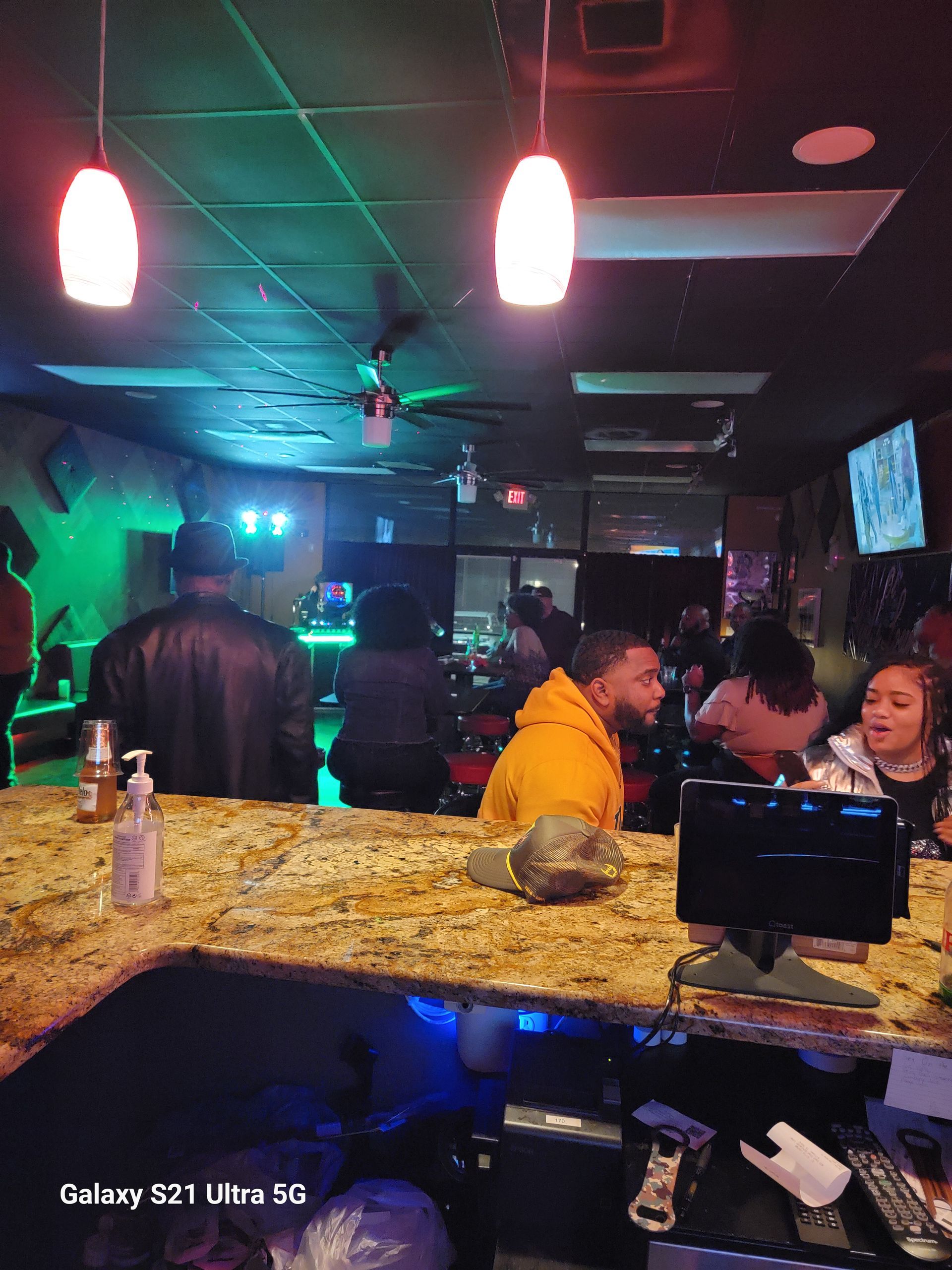 Bar interior with people, counter, and colorful lighting.