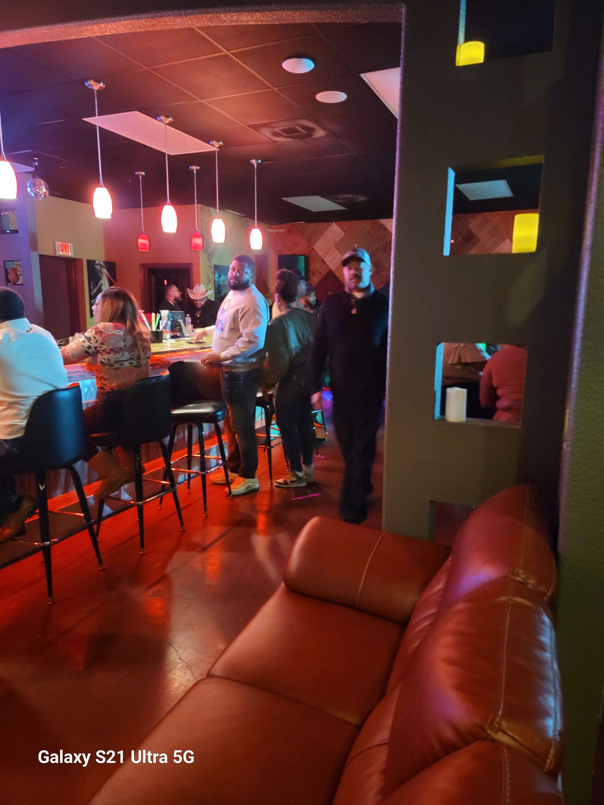 People at bar in a dimly lit establishment with red floors, red couch, and decorative lights.