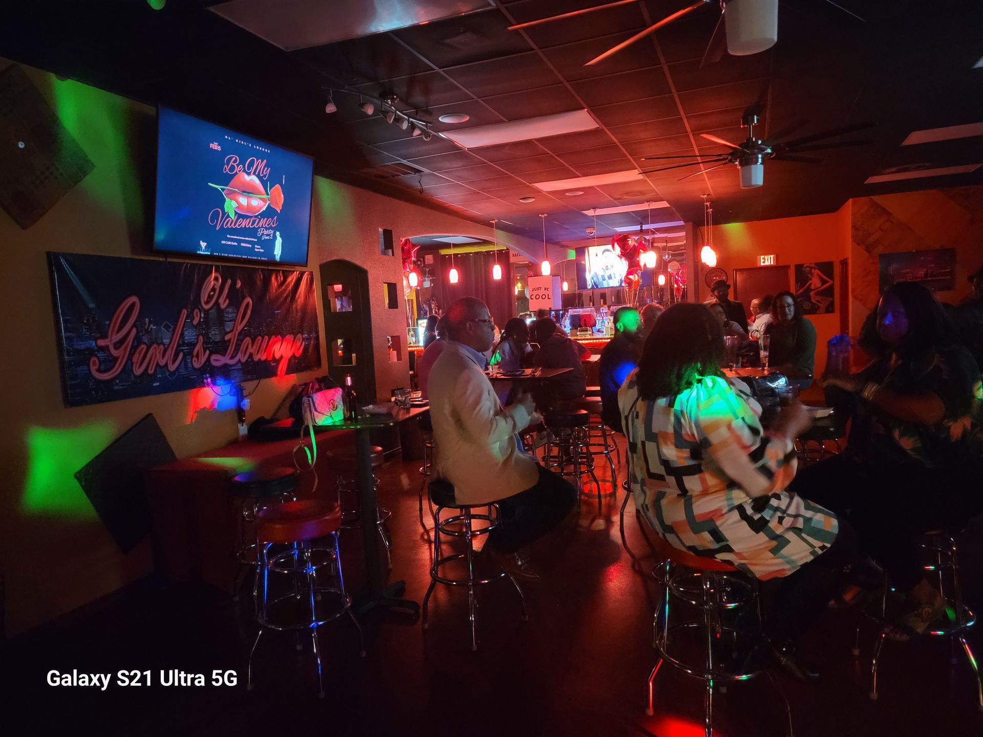 Interior of a lounge with people, red and green lighting, and a banner that says 